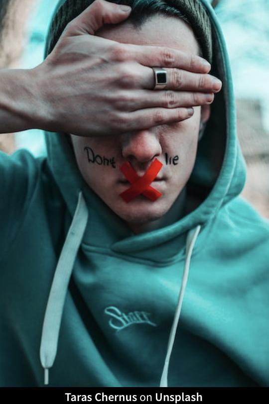 Image of a man wearing a hoodie, with his mouth taped shut and the words 'Don't lie' written on his cheeks. The photo symbolizes the challenge of dealing with liars at work. Non-verbal communication and trust issues are prominent themes, illustrating the importance of addressing lies in the workplace effectively.
